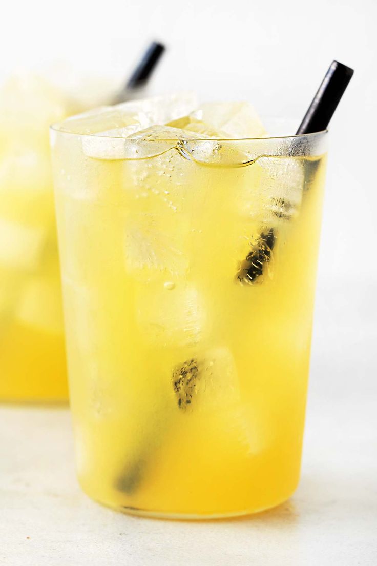 two glasses filled with lemonade and ice on top of a white table next to each other