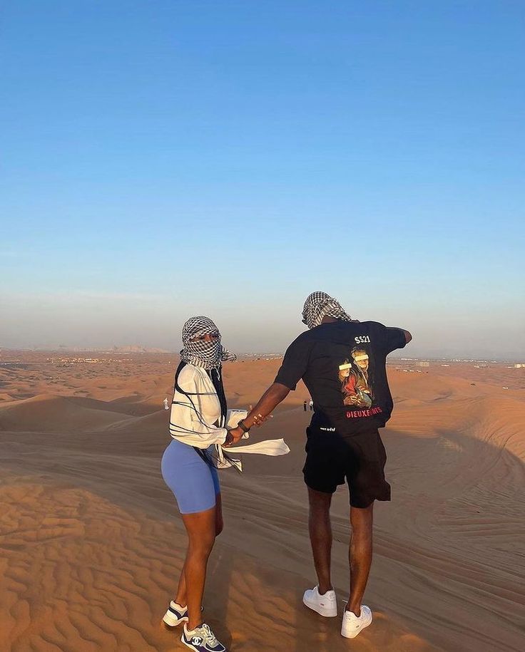 two people standing in the desert with their hands on each other's hipss