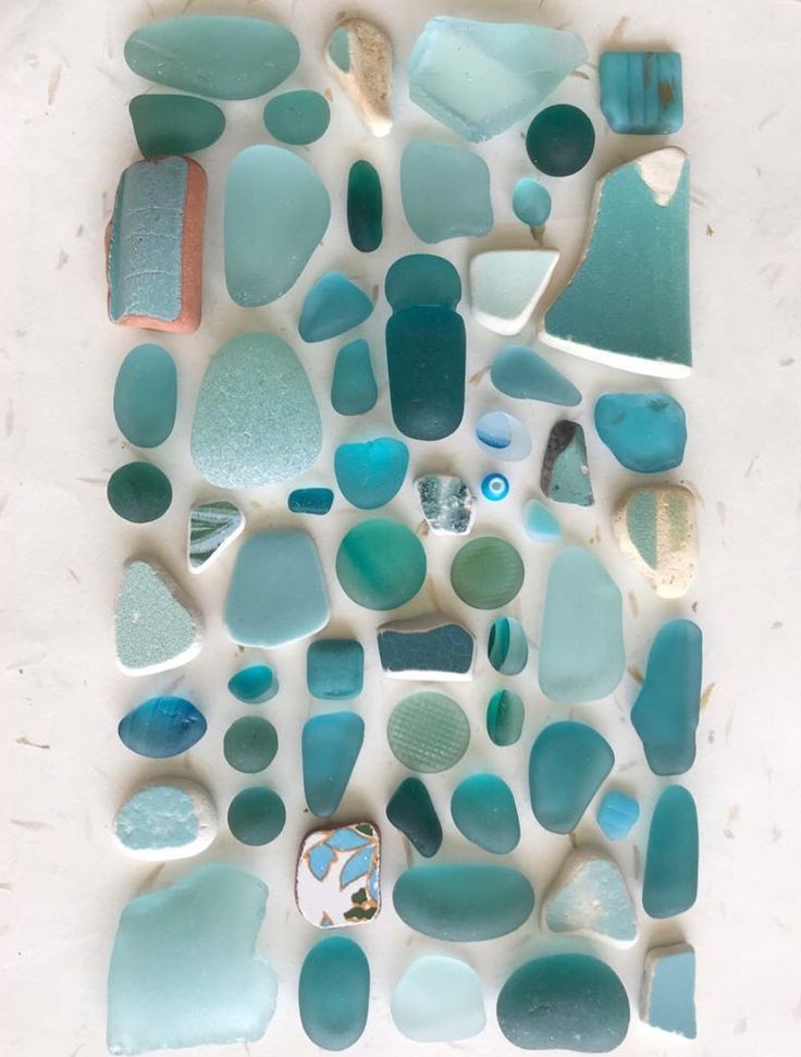 a white table topped with lots of blue and green sea glass pieces on top of each other