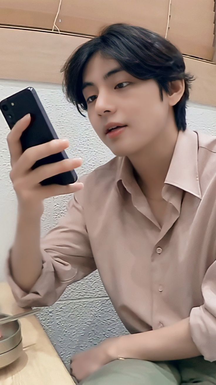 a young man sitting down while holding a cell phone in one hand and looking at the other