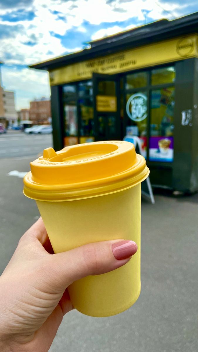 a person holding up a yellow cup in front of a store