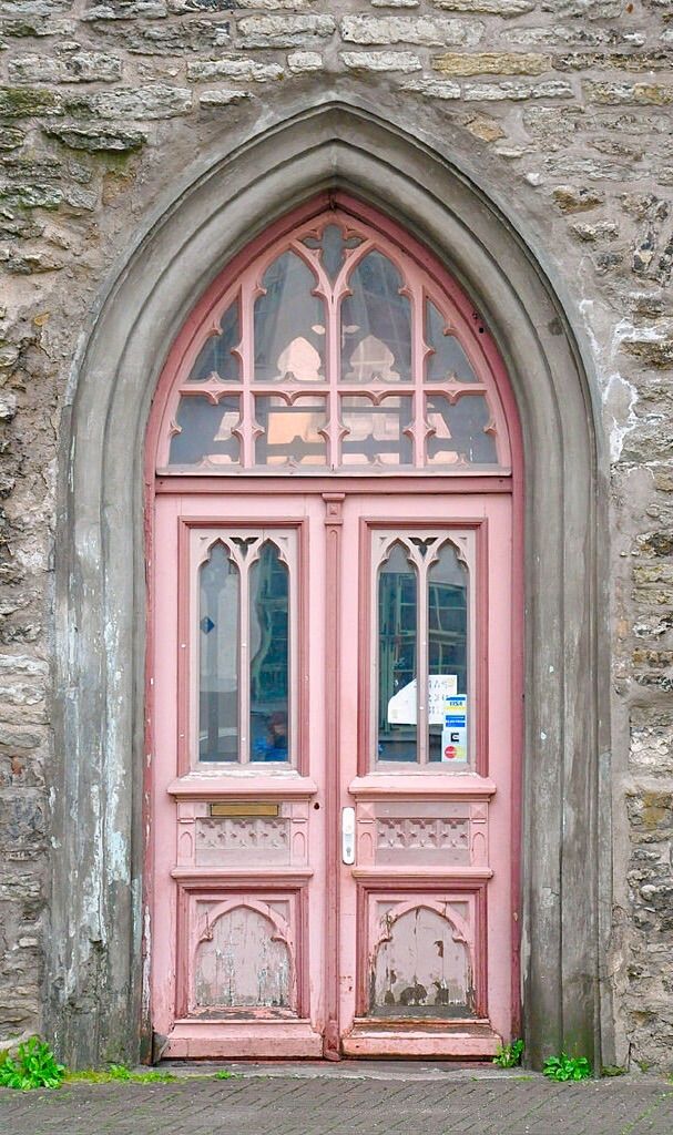 an old stone building with a pink door and arched glass window on the front side