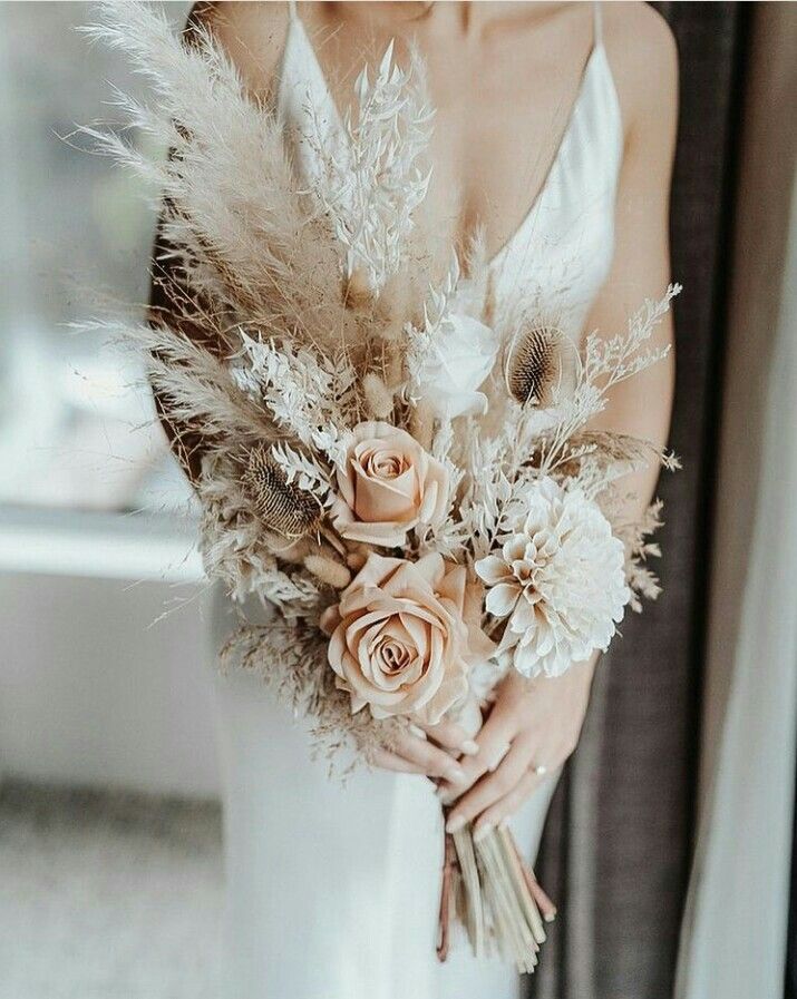 a woman in a white dress holding a bouquet of flowers and feathers on her wedding day