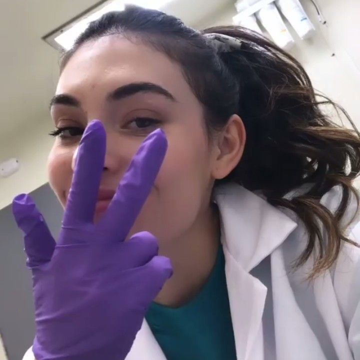 a woman wearing purple gloves and holding her hand up in front of her face while making the peace sign