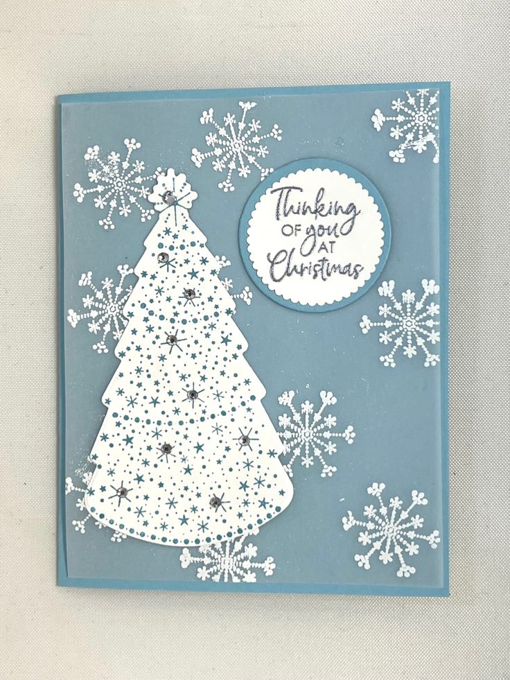 a blue christmas card with a white tree on the front and snowflakes on the back