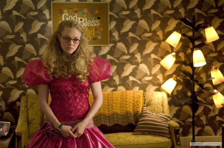 a woman in a pink dress standing next to a couch