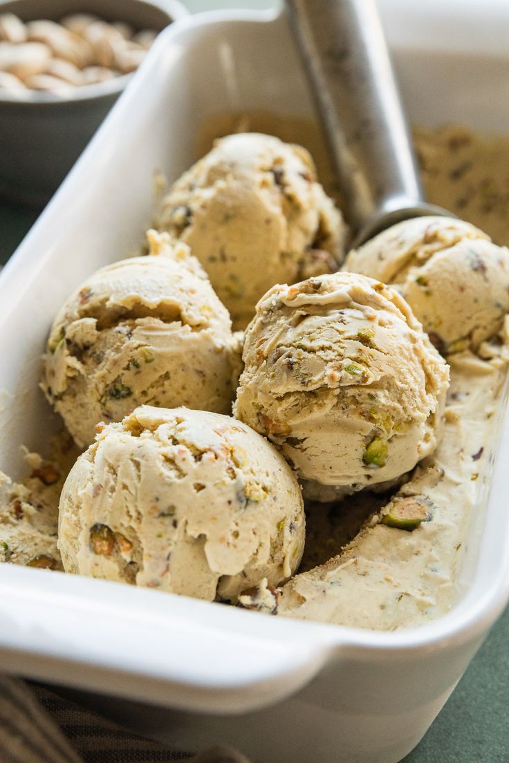 ice cream in a white container with a scoop next to nuts and a metal spoon