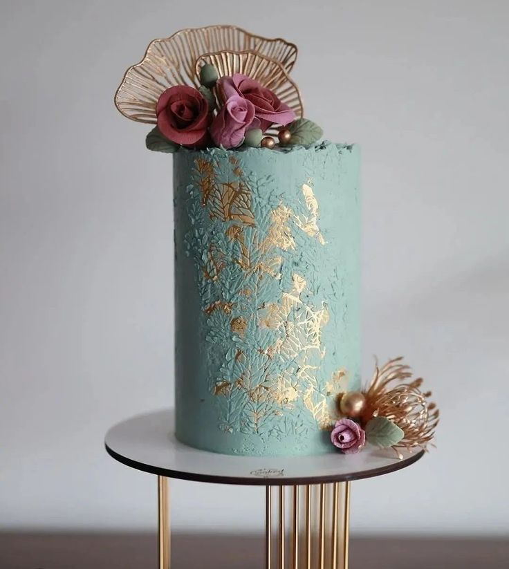 there is a blue cake with gold decorations on the top and sides, along with pink flowers