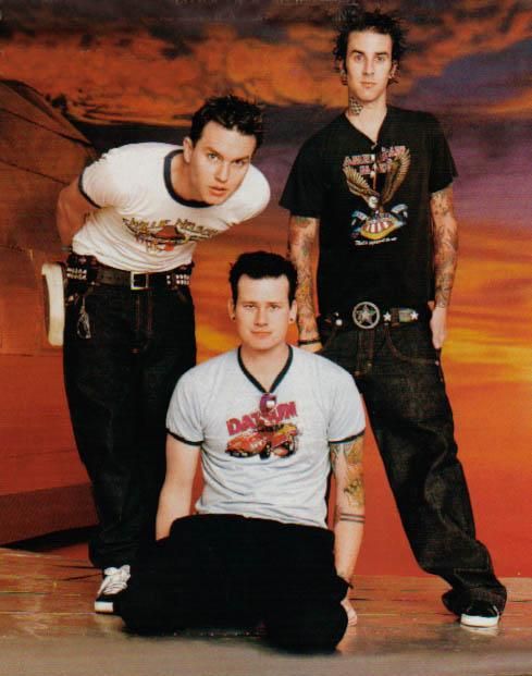 three young men posing for a photo in front of a sunset background, one is wearing a white shirt and the other wears black pants