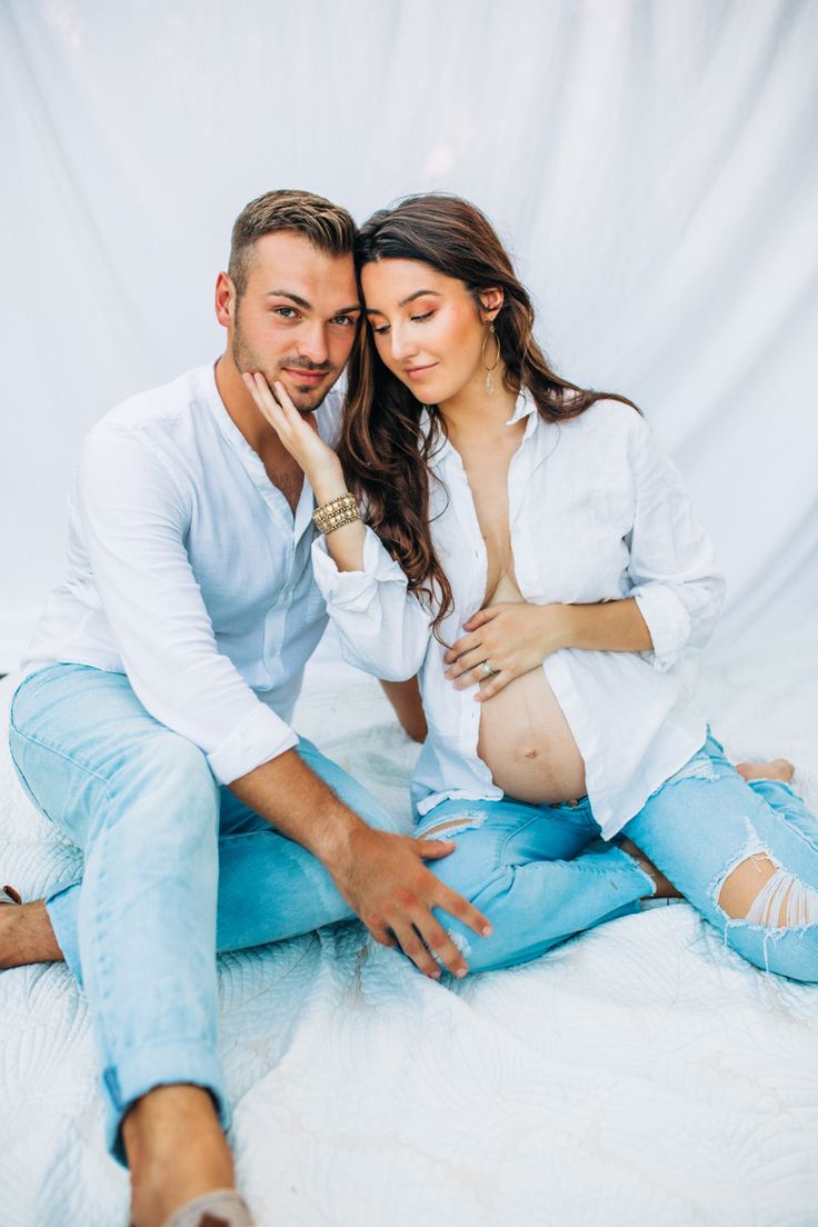 a man and woman are sitting on the bed together, posing for a photo with their hands to their face