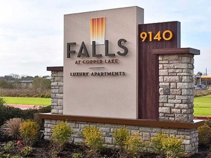 a sign for falls at copper lake luxury apartments in front of a grassy area with trees and bushes