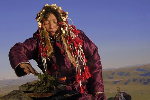 an old woman with long hair is sitting on a rock and has flowers in her hair