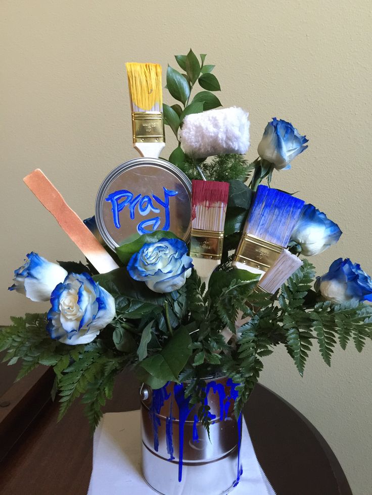 a blue and white flower arrangement with paintbrushes in a silver bucket on a table