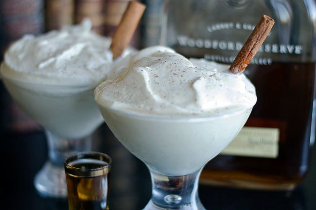 two glasses filled with ice cream and cinnamon sticks next to a bottle of whiskey on a table