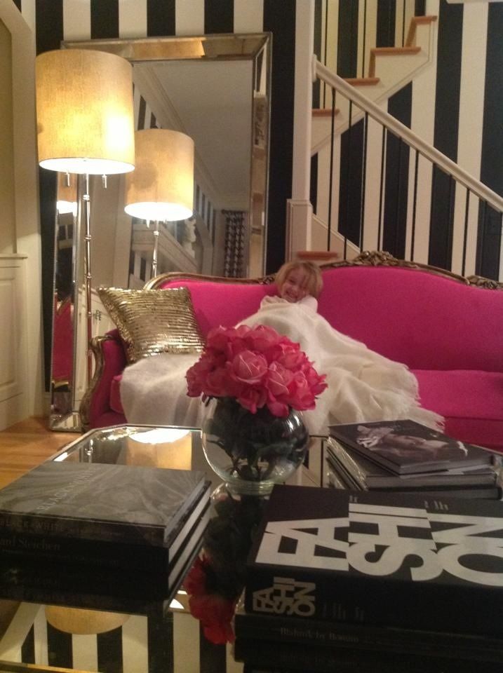 a woman laying on a pink couch in a living room with black and white striped walls