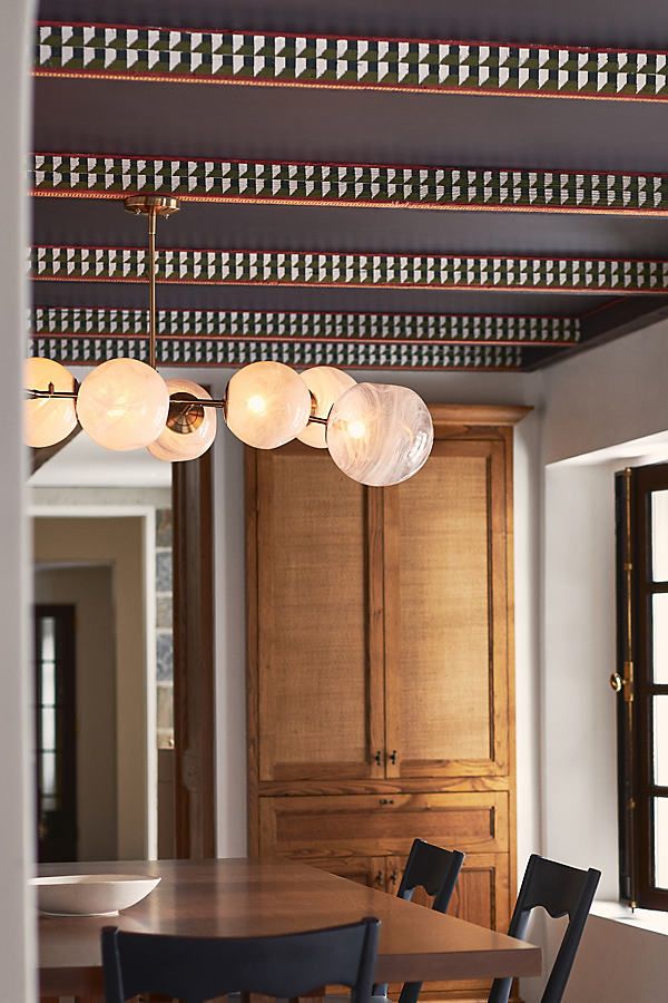 a dining room table and chairs with lights hanging from the ceiling above it, in front of wooden cabinets