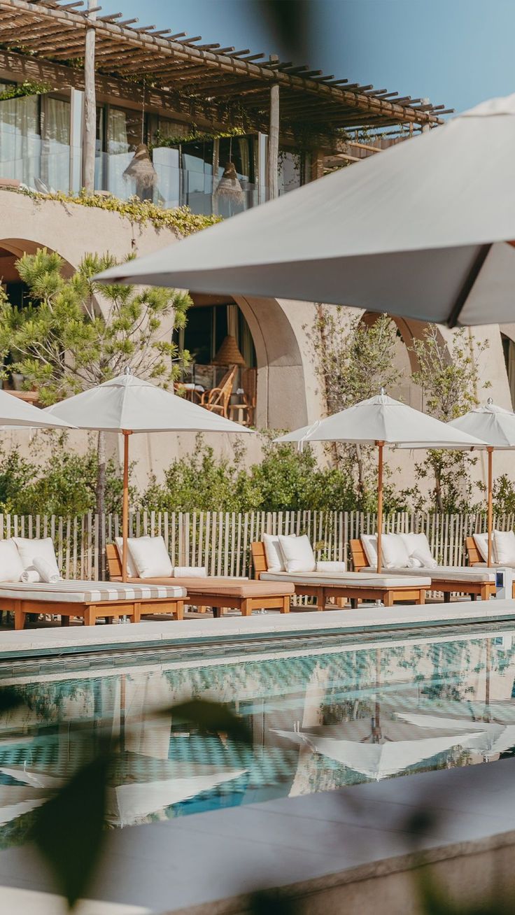 an outdoor pool with lounge chairs and umbrellas next to the side of a building