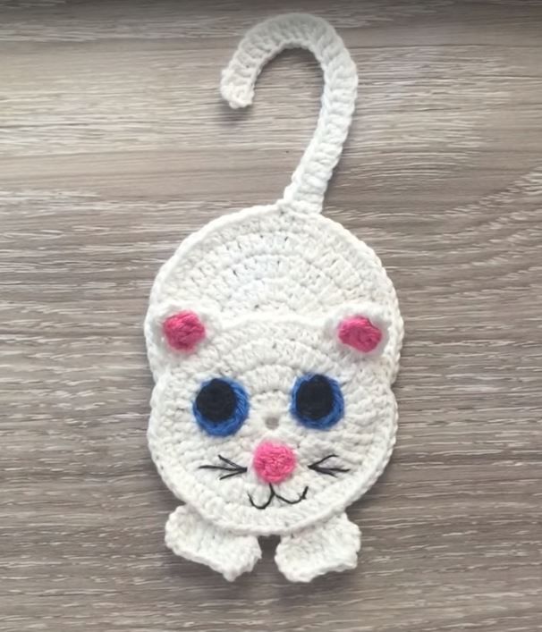 a crocheted white cat ornament hanging on a wooden surface with blue eyes and pink nose