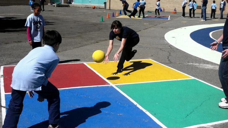 children playing with ball on colorful surface in open area near building and people standing around