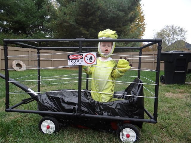 a little boy in a costume standing behind a cage