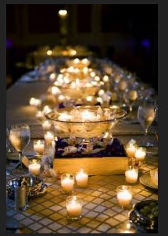 a long table with many lit candles and wine glasses on the side, along with other items