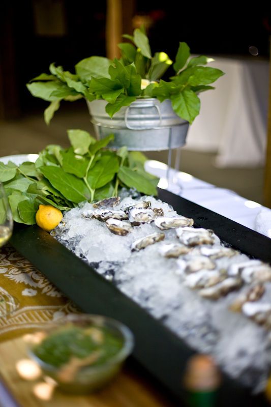 a table topped with lots of green plants and oysters on top of ice covered plates