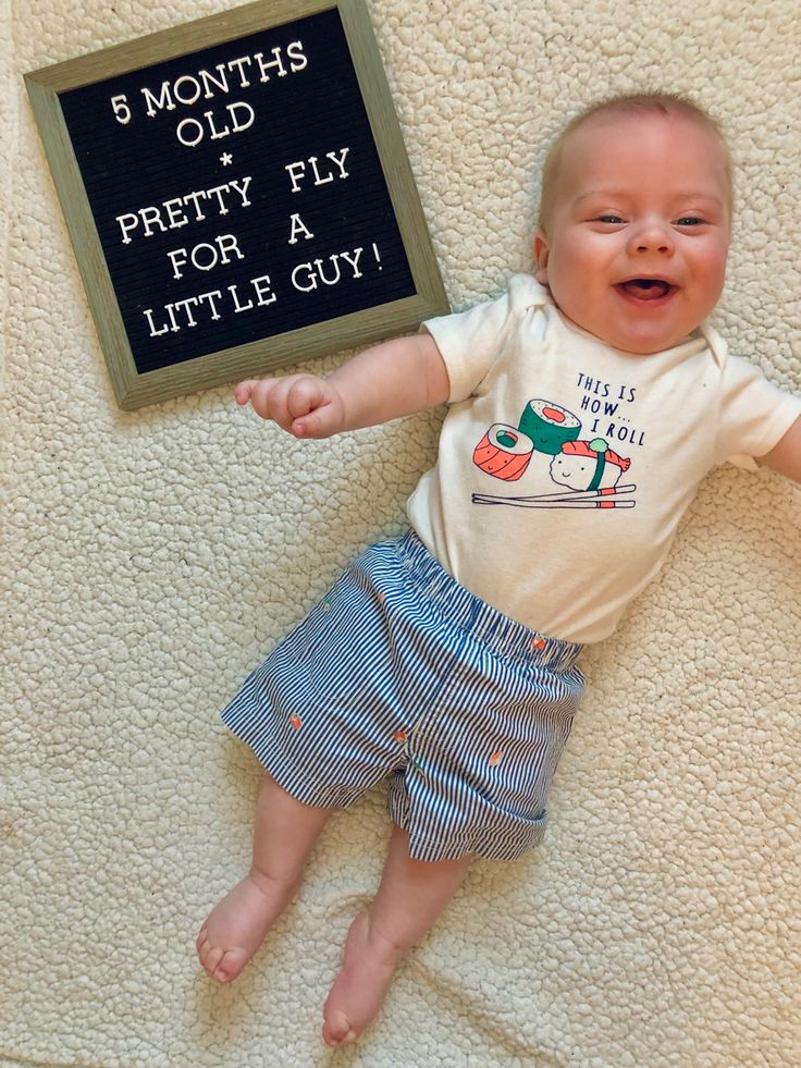 a baby laying on top of a bed next to a sign that says 5 months old pretty fix for a little guy