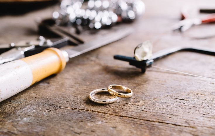 two gold wedding rings sitting on top of a wooden table next to scissors and other tools