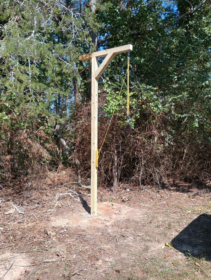 a wooden pole in the middle of a field with trees and bushes behind it on a sunny day