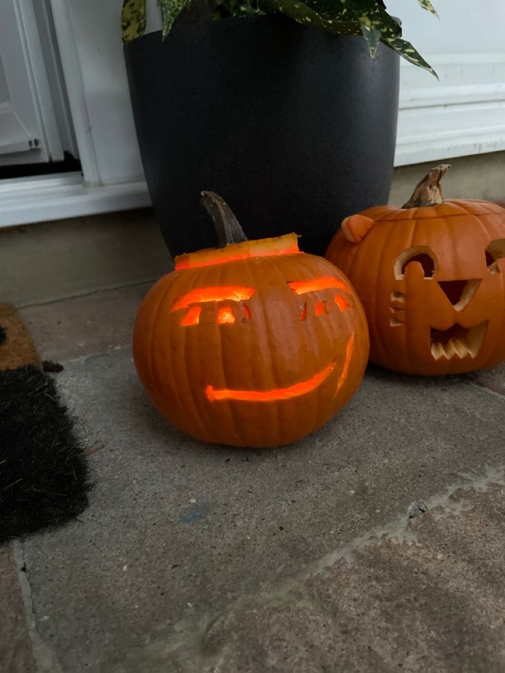 two carved pumpkins sitting on the ground next to a potted plant in front of a door