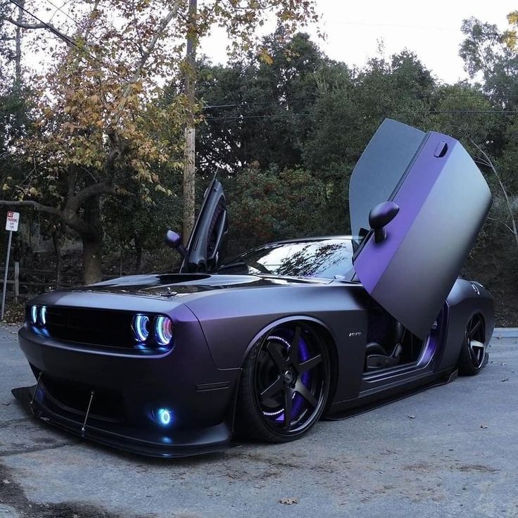 a car with its doors open sitting in a parking lot next to trees and bushes