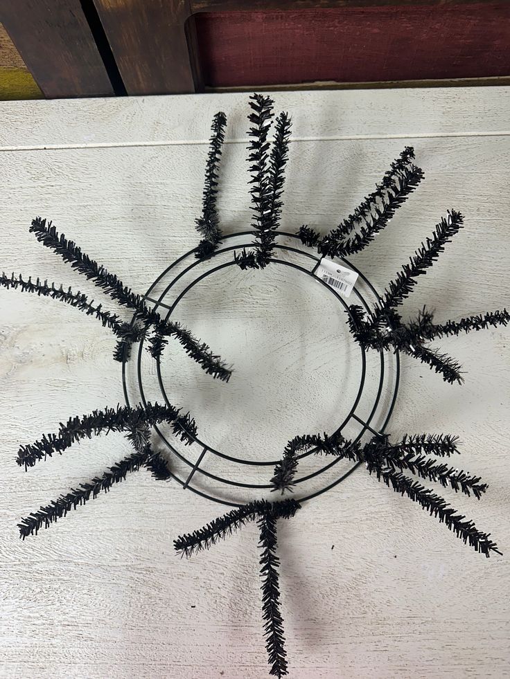 a circular metal decoration with black branches on a white tablecloth and wood planks