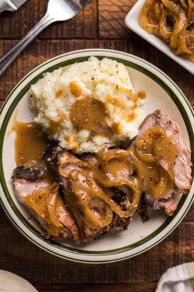 a white plate topped with meat covered in gravy and mashed potatoes on top of a wooden table