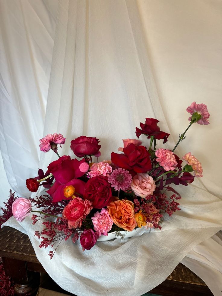 a bunch of flowers that are sitting on a table in front of a white curtain