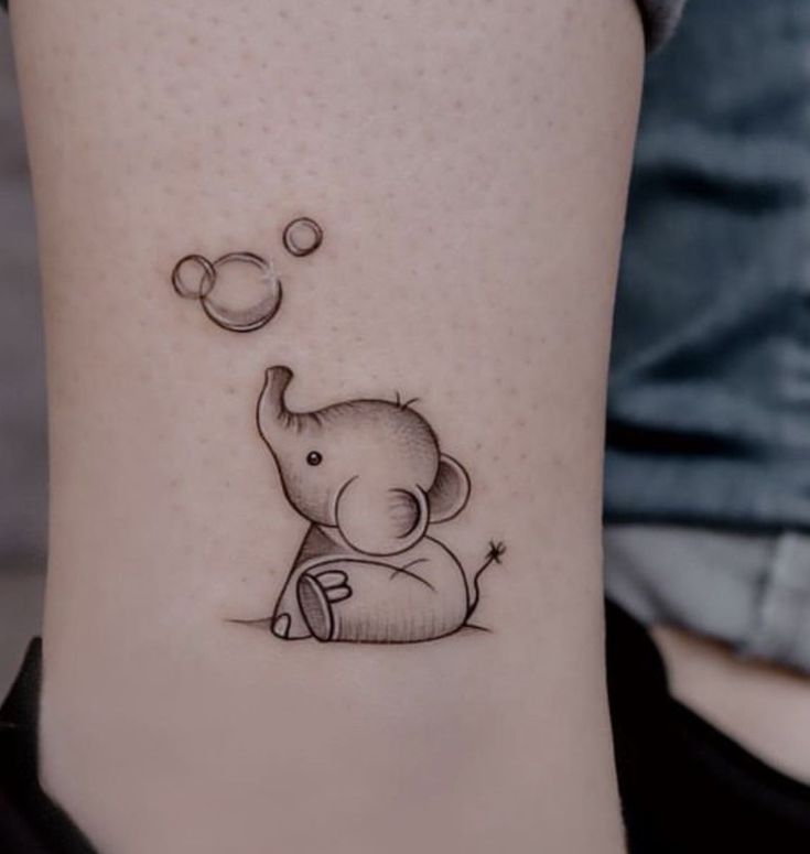 small elephant tattoo on the ankle with bubbles coming out of its trunk and an object floating in the air