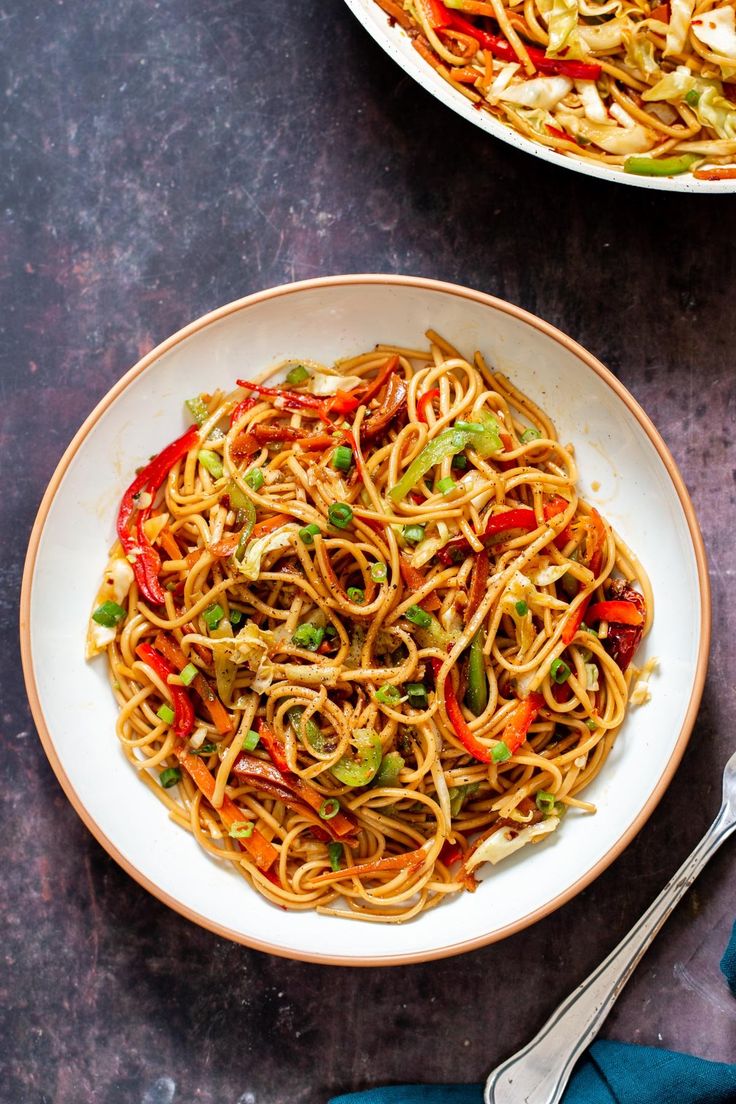 two bowls filled with noodles and vegetables on top of a black table next to silverware