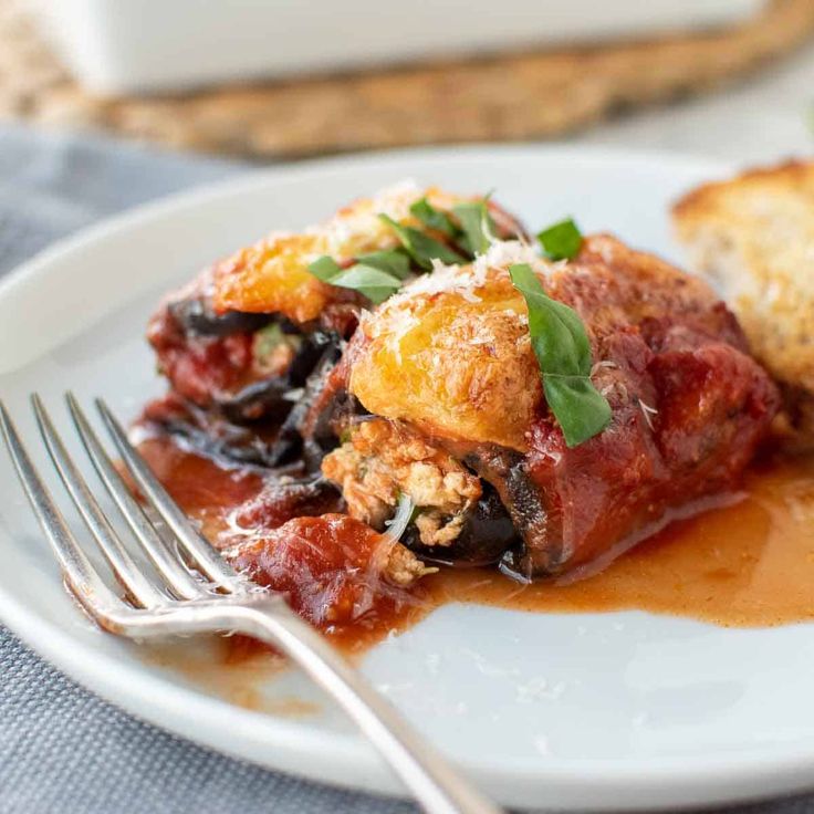 a white plate topped with lasagna covered in sauce and garnished with parmesan cheese