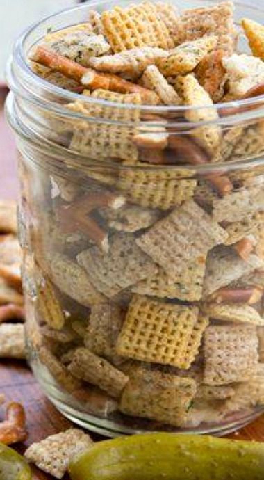 a glass jar filled with chex mix next to a pickle and crackers