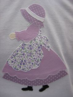 a white t - shirt with a purple dress and hat embroidered on the chestline