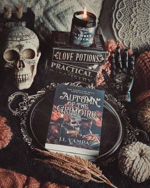 a table topped with books and skulls on top of a cloth covered bed next to a candle