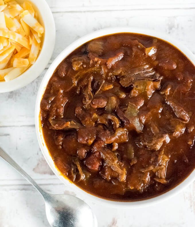 a bowl of beef and potato stew next to a plate of chips on a white table