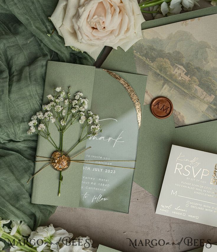 the wedding stationery is laid out on top of the green sheets and flowers, including roses