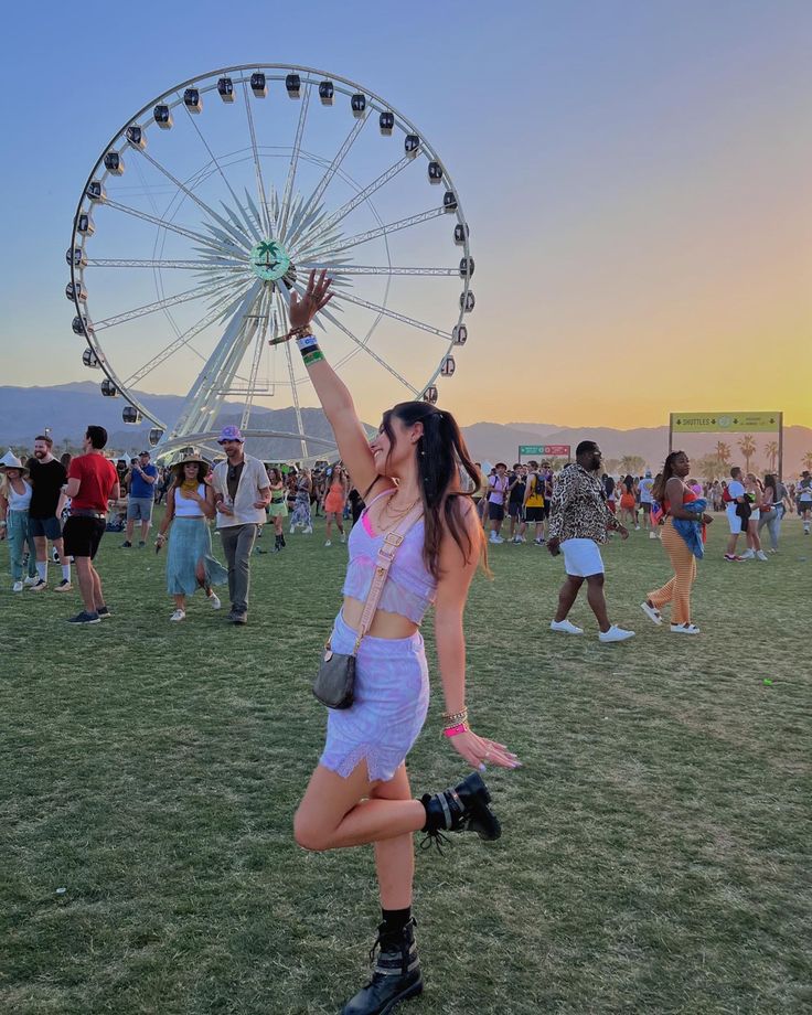 a woman is dancing in front of a ferris wheel at an outdoor music festival with other people