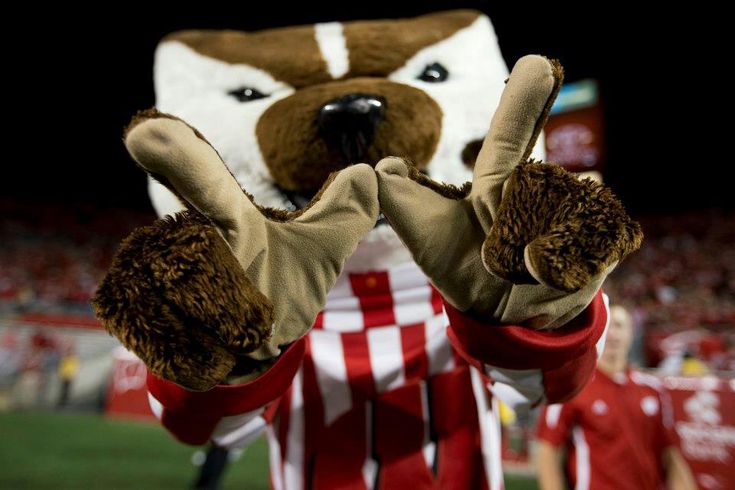 a mascot with his hands in the air at a soccer game, wearing gloves and holding up two fingers