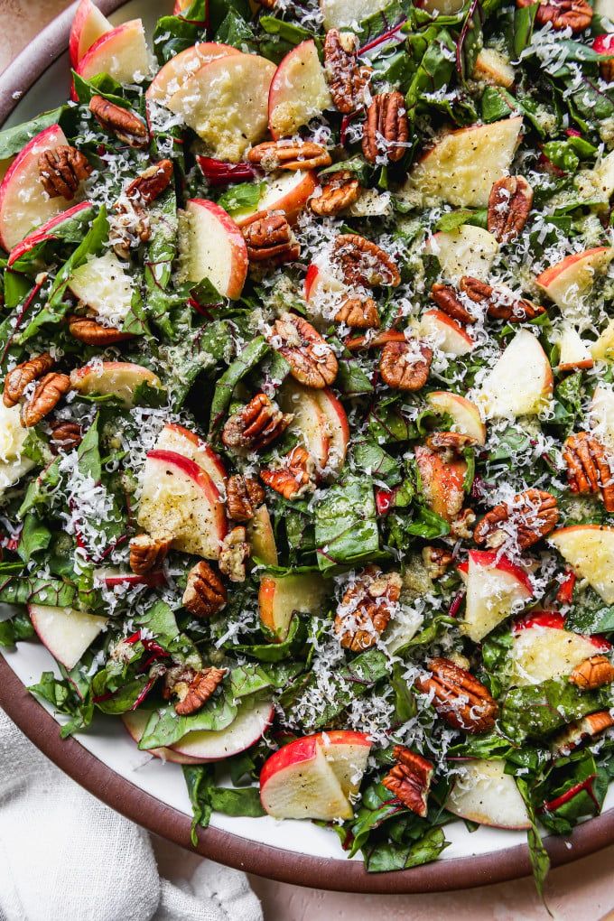 a salad with apples, spinach and pecans in a bowl on a table