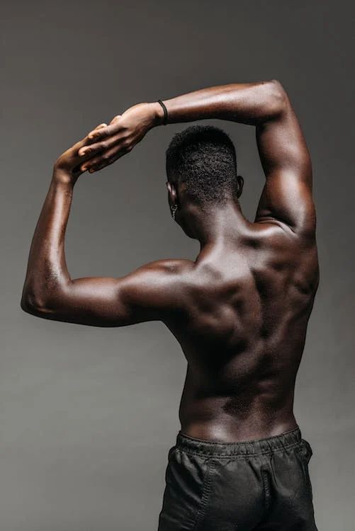 a man with no shirt on is holding his hands up to his head while standing in front of a gray background