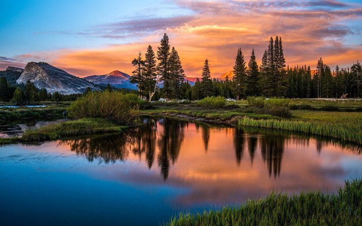 a beautiful sunset over a mountain lake with trees in the foreground and mountains in the background