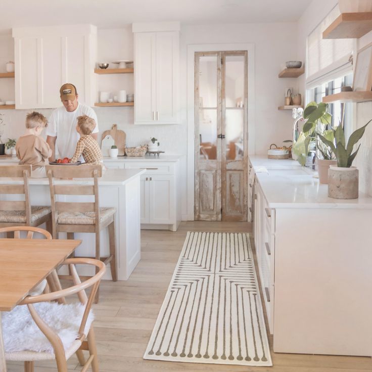 a man and two children standing in a kitchen with white cabinets, wood floors and an area rug on the floor