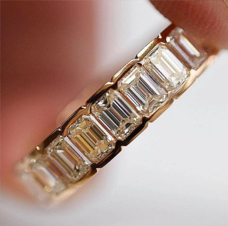 a close up of a person's hand holding a gold ring with baguettes