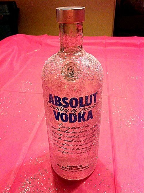 a bottle of absolut vodka sitting on a pink table with glitter around it